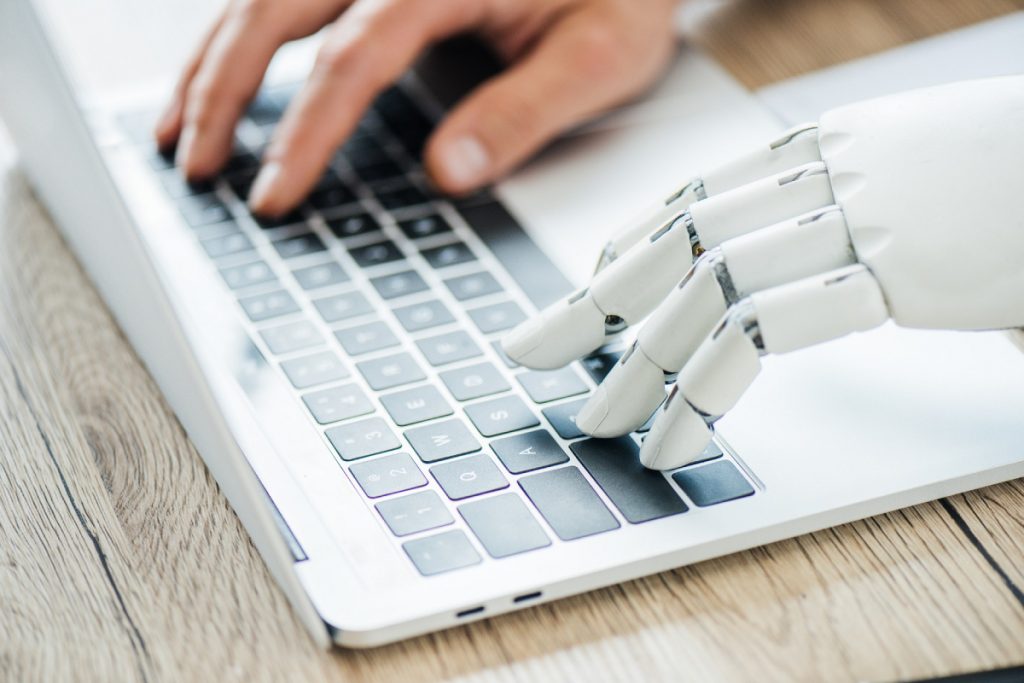 Human and robot hand typing on a laptop